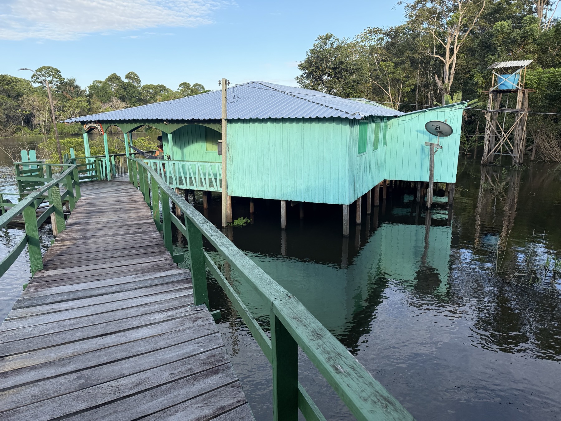 The mint-green wooden pousada on stilts above the river, reached by a wooden walkway