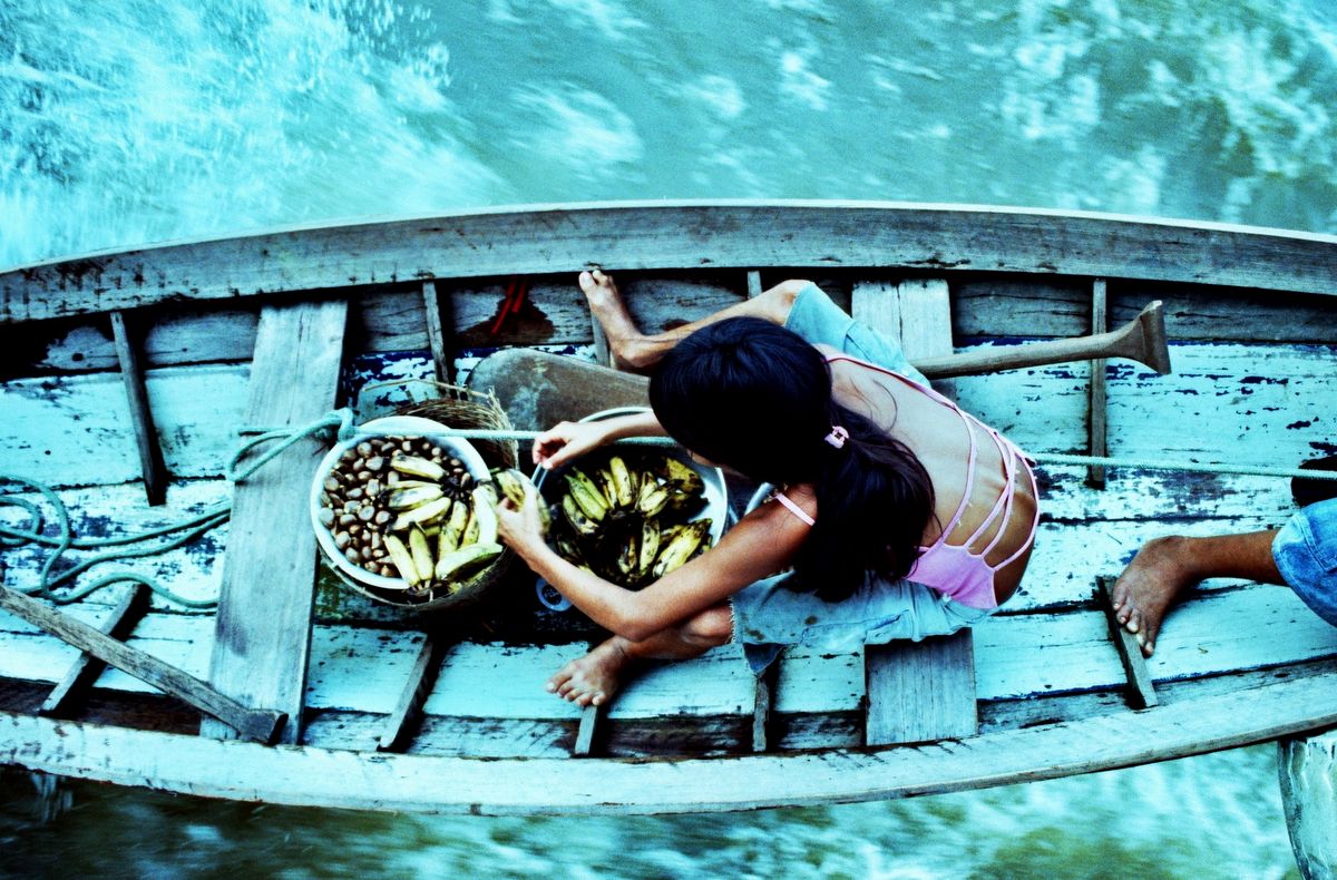 A woman trading bananas and nuts from a wooden canoe